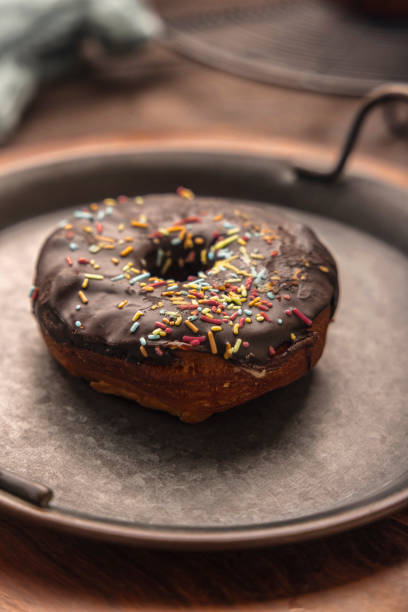 istock Chocolate frosted donut with colourful festive sprinkles kept in rustic iron plate 1292712633