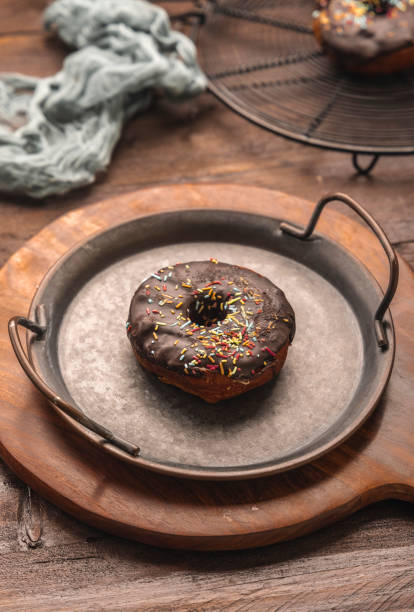 Chocolate frosted donut with colourful festive sprinkles kept in rustic iron plate