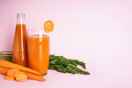 Fresh carrot juice in a glass cup and fresh carrots on a pink background. Space for text.