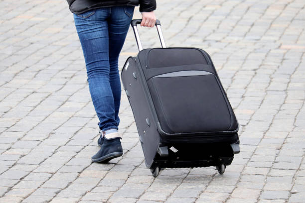 Woman in jeans walking with a suitcase on wheels Female legs and luggage on the cobbled street, back view. Concept of travel, hurrying or late travelers wheeled luggage stock pictures, royalty-free photos & images