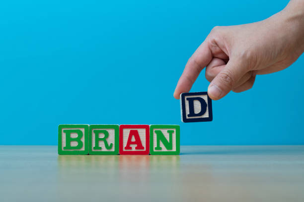 Human hand spelling word brand with toy blocks.