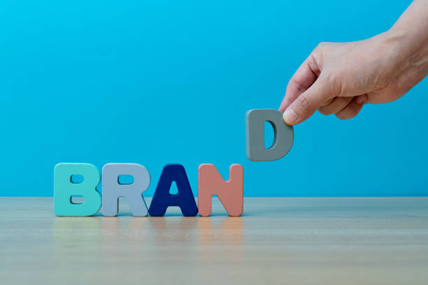 Human hand spelling word brand with toy blocks.