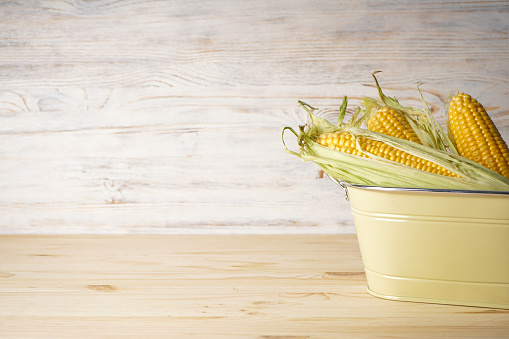 Ripe ears of corn in a basket on a wooden background, space for text.