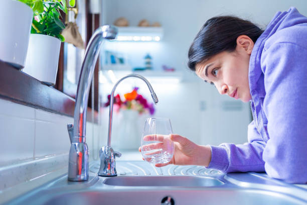 giovane e preoccupata donna è in attesa di un'ultima goccia d'acqua pende da un rubinetto con vetro sotto carenza d'acqua colpito dalla siccità . carenza idrica e crisi della siccità con il riscaldamento globale - house home interior water glass foto e immagini stock