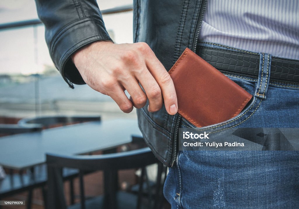 Men's hand wallet in the pocket The man pulls a brown leather wallet out of his jeans pocket Wallet Stock Photo