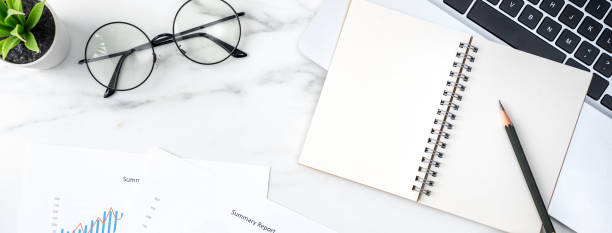 istock Office table desk work with blank notebook, report and alarm clock on marble white background. 1292721568