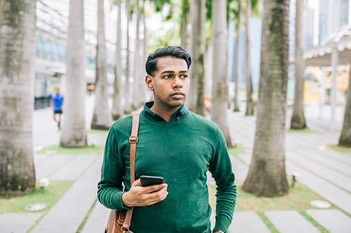 Indian man walking through the city to work, wearing shoulder bag.