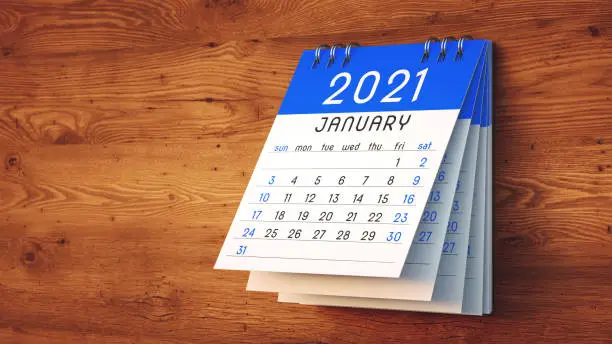 Curled up 2021 calendar blue note pad stack with January front page hanging on a bright wooden wall