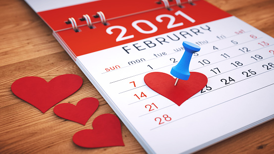 Extreme close-up on an open 2021 calendar note pad February page with pinned symbolic hearts