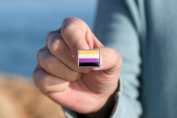 person showing a non-binary pride flag closeup of a young caucasian person showing a lapel pin patterned with a non-binary pride flag non binary gender stock pictures, royalty-free photos & images