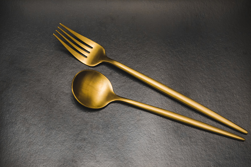 The spoon and fork are gold on a dark gray background.