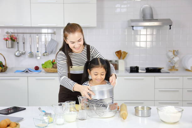 happy asian mother teaching her young daughter to bread baking in white modern kitchen while sieving wheat flour - bun bread 7 grain bread dough imagens e fotografias de stock