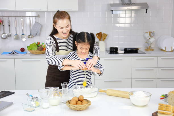 feliz madre asiática enseñando a su hija pequeña rompiendo huevo para mezclar con harina a pan hornear en la cocina blanca - bun bread 7 grain bread dough fotografías e imágenes de stock