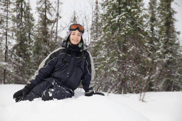 retrato de una chica sonriente sentada en la nieve con monos y gafas de esquí - mono ski fotografías e imágenes de stock