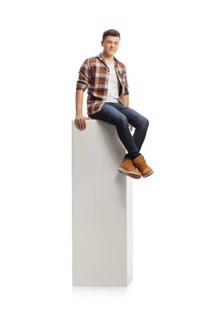 istock Teenag guy sitting on a white column and smiling at camera 1292732222