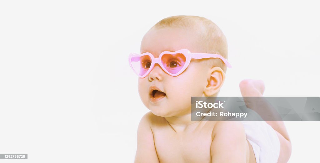 Portrait of little baby wearing a summer pink heart shaped sunglasses and diapers looking away over a white background 2-5 Months Stock Photo