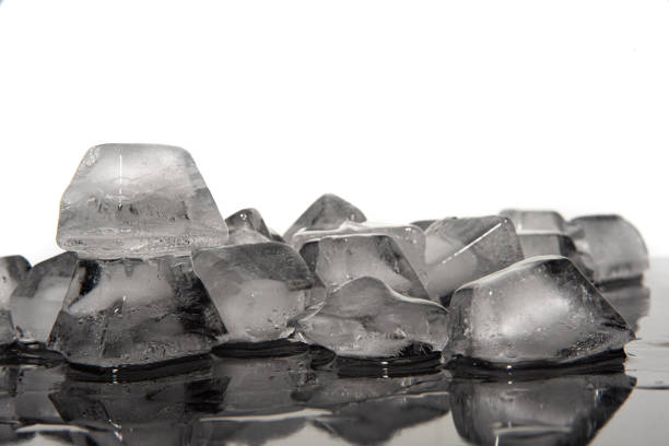 istock Ice cubes melting on dark reflective surface, white background, selective focus. 1292740300