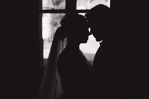 Silhouette of groom and bride in front of window.