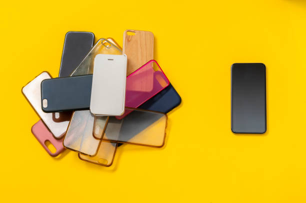 istock Pile of multicolored plastic back covers for mobile phone on yellow background. Choice of smart phone protector accessories. A lot of silicone phone backs or skins next to smart phone 1292740439