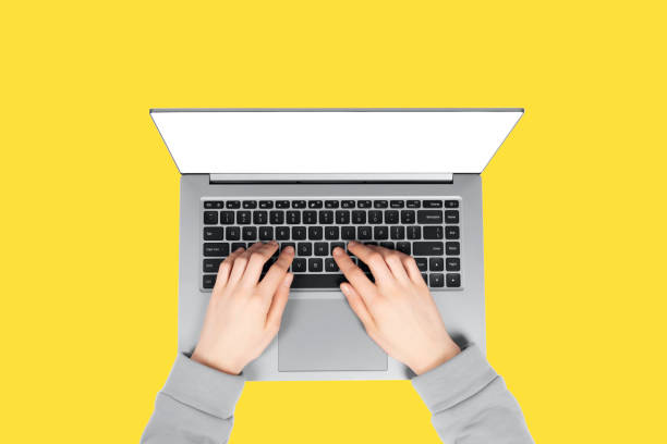 istock Person working on a laptop computer in a modern space. Female hands working on new laptop with blank screen isolated on illuminating yellow background. 1292741710