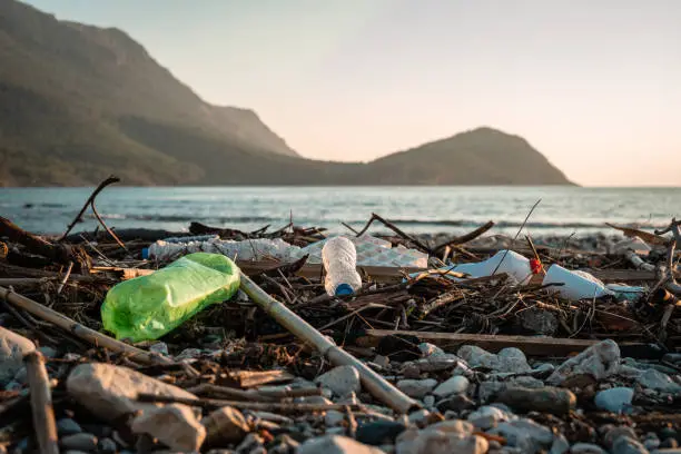 Sunset in the Mediterranean. Mountains and sea on the shore. Plastic bottles hitting the beach. Environmental problem