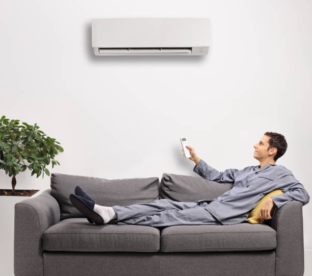 istock Young man in pajamas with a remote control putting on an air conditioning unit 1292744612