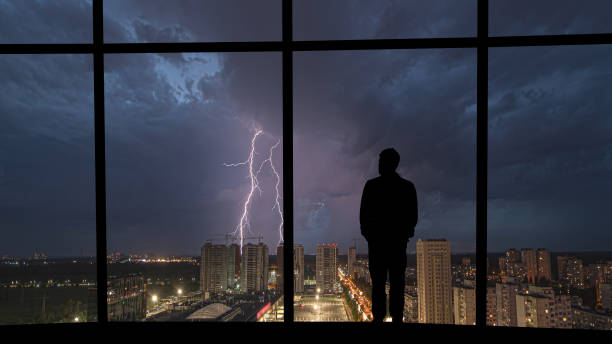 der mann, der in der nähe des panoramafensters auf dem nächtlichen blitzhintergrund steht - lightning thunderstorm city storm stock-fotos und bilder