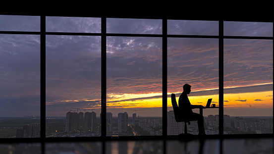 The businessman sitting near a panoramic window with a city sunset