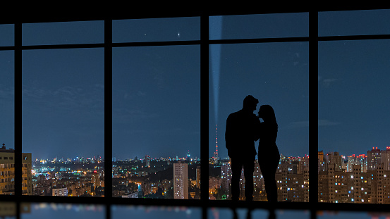 The couple standing near the panoramic window on the city background