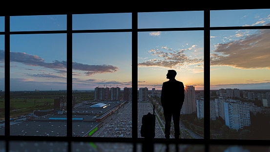 The man with a suitcase standing near the panoramic window with a sunset