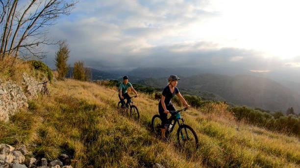 gli appassionati di mountain bike cavalcano attraverso un prato erboso al mattino - morning italy shadow sunlight foto e immagini stock