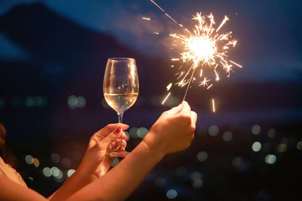 jovem celebra véspera de ano novo com faíscas e vinho - sparkler sparks new years eve human hand - fotografias e filmes do acervo