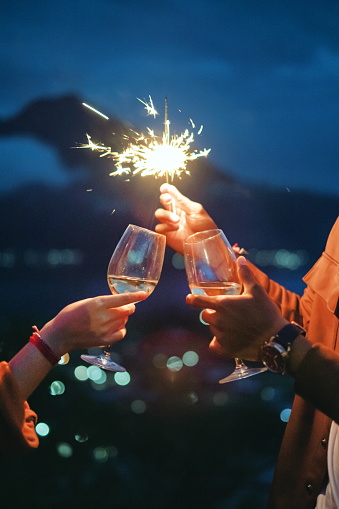 Close up shot of Asian couple toasting white wine underneath a sparkler at night time during new year's eve celebration, with a scenic view of mount Batur in Bali