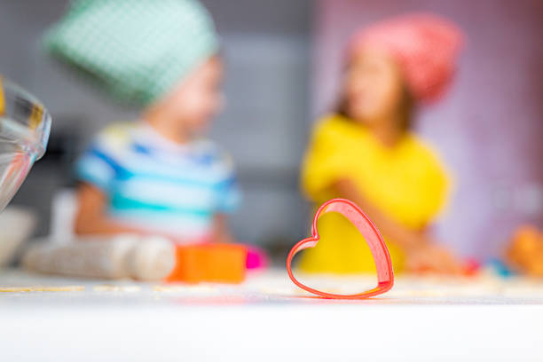 A heart-shaped metallic cookie cutter cuts out cookie dough into heart shapes for homemade Valentine's day cookies.