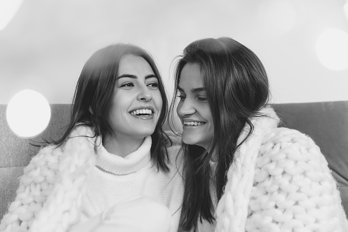 Laughting. Portrait of beautiful brunette women in comfortable soft longsleeves on studio background, black and white. Home comfort, emotions, facial expression, winter mood concept. Friendship.