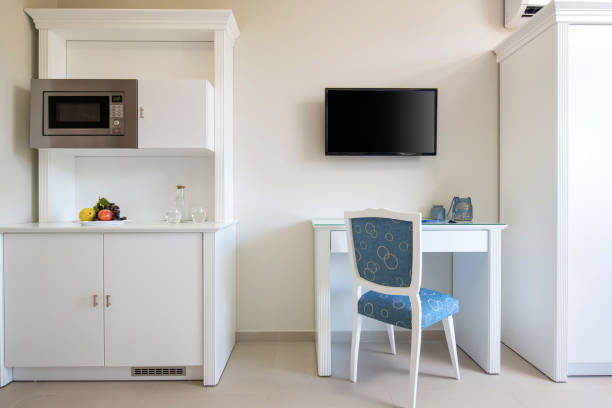 vista frontal de la pared blanca con tv, mesa, silla azul clásica, armario de madera de la cocina con electrodomésticos incorporados en el interior moderno de la habitación pequeña - small domestic kitchen apartment rental fotografías e imágenes de stock