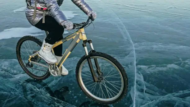 Photo of Woman is riding bicycle on the ice. Tires on bike are covered wi