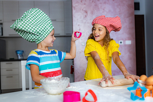 Boy and girl whit chef hat making cookies in the kitchen