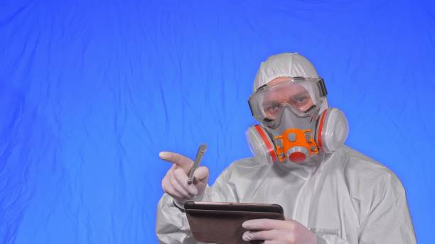 istock Scientist virologist in respirator makes write in an tablet computer with stylus. Man wearing protective medical mask. Chroma key blue. 1292761978