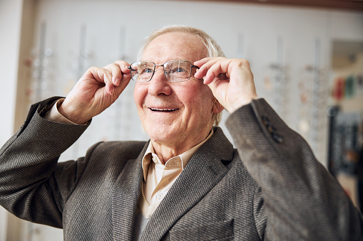 Portrait of a smiling contented Caucasian male customer putting on a new pair of eyeglasses