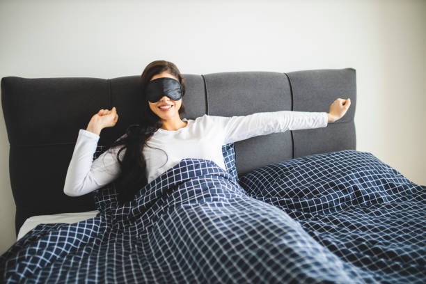 istock Young woman wearing sleeping mask and stretching while sitting in her bed 1292768332