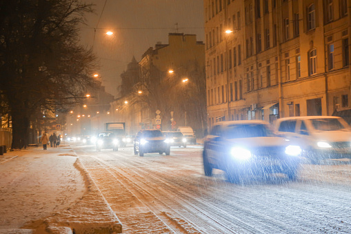 cars driving on city road on winter evening during snowfall