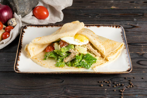 repe com salada e ovo. prato principal quente para o café da manhã ou almoço de panquecas com ovo frito, filé de frango, legumes e salada em um prato de cerâmica em uma mesa de cozinha de madeira. - salad caesar salad main course restaurant - fotografias e filmes do acervo