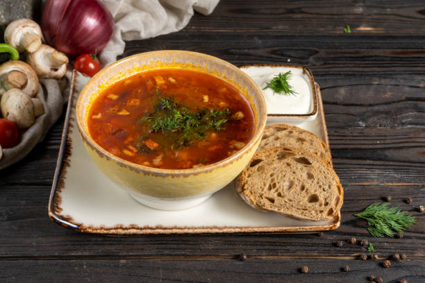 istock Solyanka. Traditional Russian soup made from vegetables, bacon and herbs in a ceramic plate with sour cream and rye bread on a wooden kitchen table. Hodgepodge 1292770153