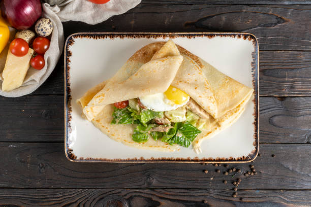 istock repe with salad and egg. Hot main course for breakfast or lunch of pancakes with fried egg, chicken fillet, vegetables and salad in a ceramic plate on a wooden kitchen table. 1292770262
