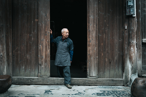 Old chinese senior man looking out of the door of old wooden house in daxu ancient town