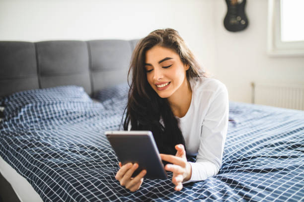 istock Young woman using digital tablet while lying on bed at home 1292771681