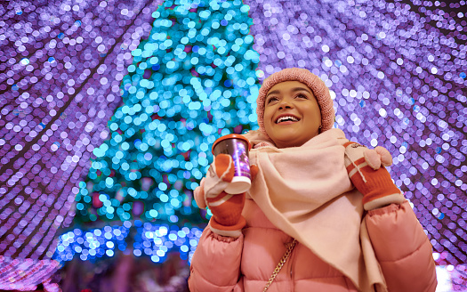 Happy young girl smiling and drink coffee in front of the christmas tree. New year concept. Impressive christmas tree with garland