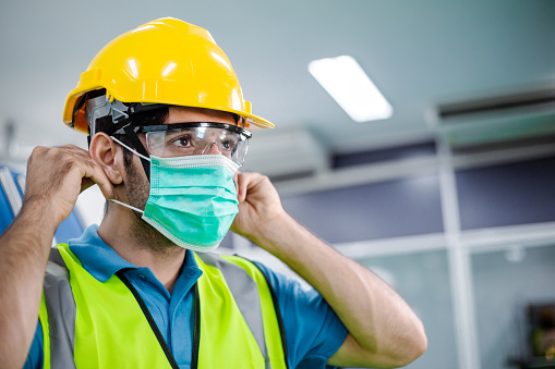 Portrait of male engineer worker wearing protective face mask, safety helmet and glasses at factory. industrial plant and new normal working. man standing and look forward, copy space