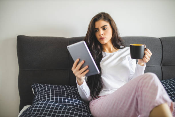istock Beautiful young woman reading magazine on digital tablet and drinking coffee while sitting in bed at the morning 1292773344
